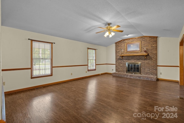 unfurnished living room with dark wood-style floors, lofted ceiling, a ceiling fan, a brick fireplace, and a textured ceiling