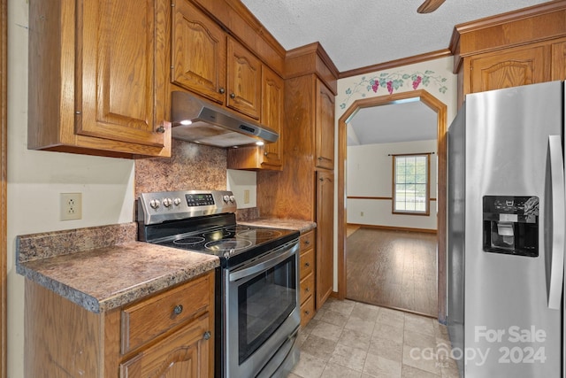 kitchen featuring brown cabinetry, dark countertops, appliances with stainless steel finishes, a textured ceiling, and under cabinet range hood