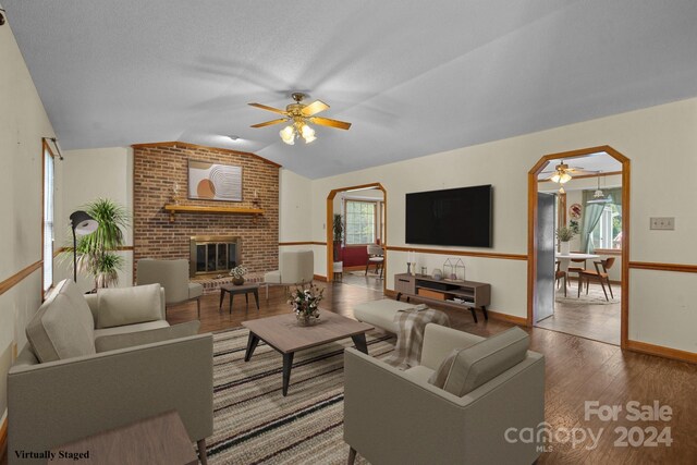 living room featuring ceiling fan, brick wall, a brick fireplace, hardwood / wood-style flooring, and lofted ceiling