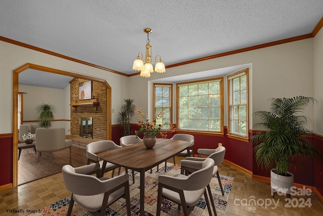 dining space with crown molding, a notable chandelier, a brick fireplace, wainscoting, and a textured ceiling