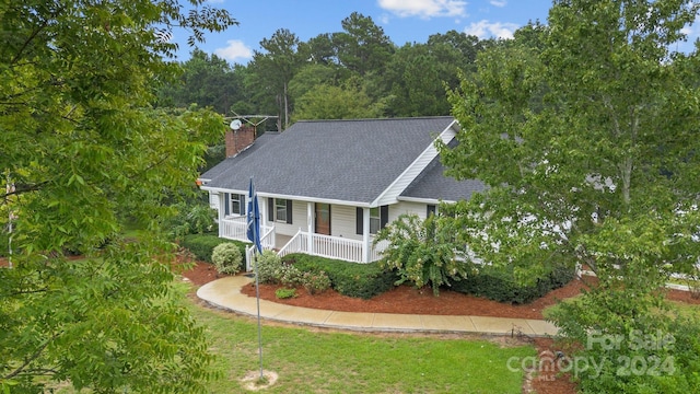 view of front of house with roof with shingles, a porch, a chimney, and a front yard