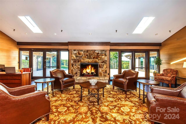 living room with a stone fireplace, lofted ceiling with skylight, wood walls, and french doors