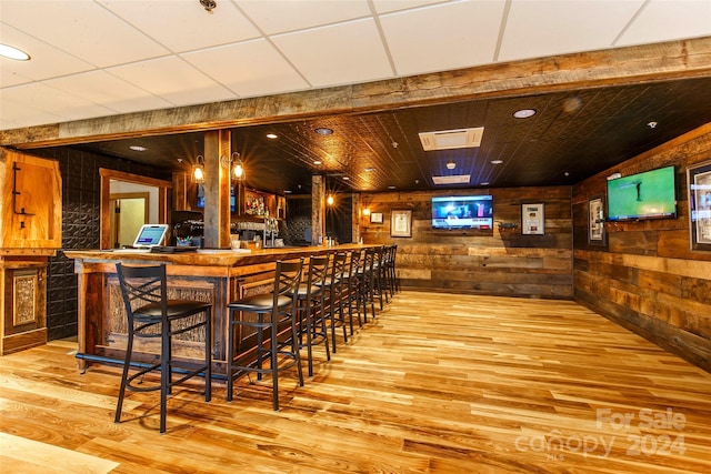 bar featuring decorative light fixtures, light hardwood / wood-style flooring, and wooden walls