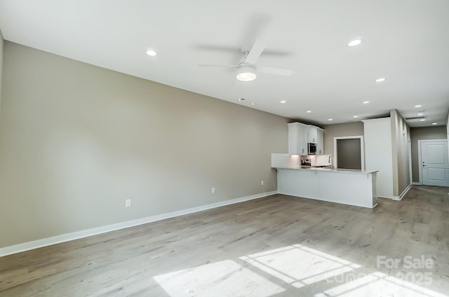 interior space with light hardwood / wood-style floors, white cabinetry, sink, kitchen peninsula, and ceiling fan