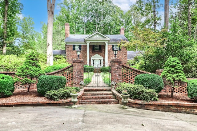 greek revival house with a gate, brick siding, and a chimney