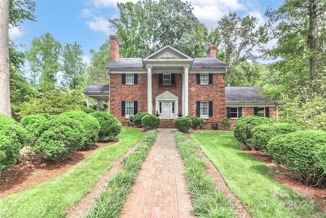 greek revival house featuring brick siding, a chimney, and a front yard