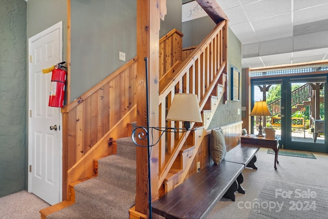 stairway with french doors, carpet floors, and a drop ceiling