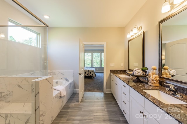 bathroom with vanity, a relaxing tiled tub, and plenty of natural light