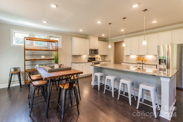 kitchen featuring stainless steel appliances, decorative light fixtures, an island with sink, and white cabinets