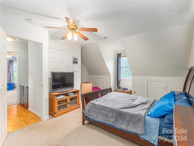 bedroom with a textured ceiling, ceiling fan, light colored carpet, vaulted ceiling, and a closet