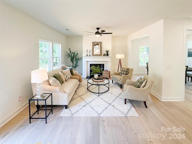 living room with a tile fireplace, ceiling fan, and light hardwood / wood-style floors