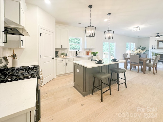 kitchen featuring ceiling fan with notable chandelier, gas stove, white cabinetry, a center island, and light hardwood / wood-style floors