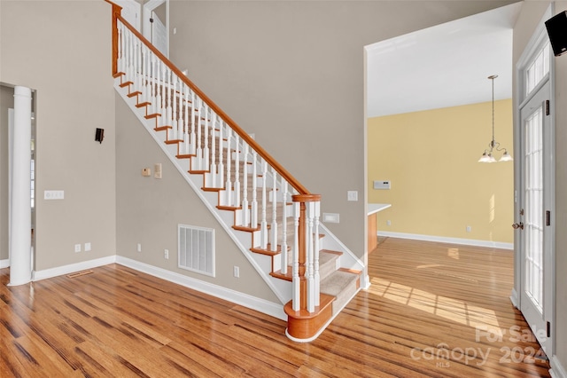 staircase with hardwood / wood-style floors, an inviting chandelier, and a high ceiling