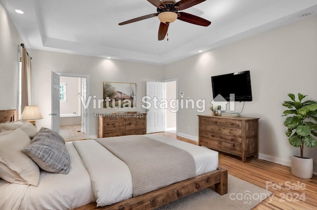 bedroom with a tray ceiling, ceiling fan, light hardwood / wood-style floors, and ensuite bathroom