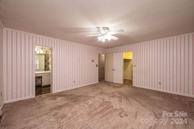 unfurnished bedroom featuring ensuite bathroom, crown molding, a walk in closet, carpet floors, and ceiling fan