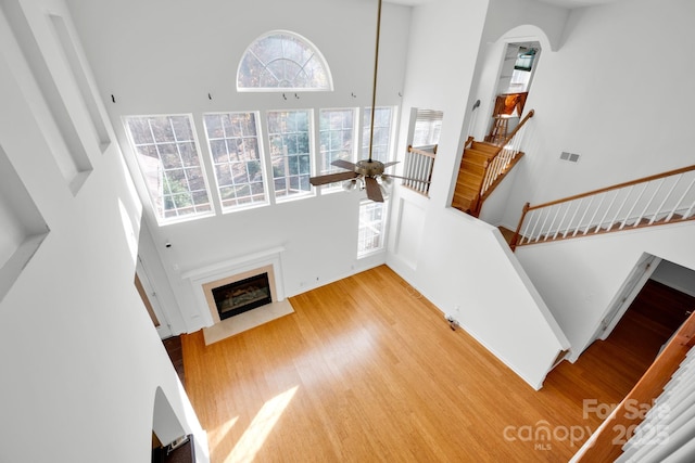 staircase featuring a high ceiling, ceiling fan, hardwood / wood-style flooring, and a fireplace