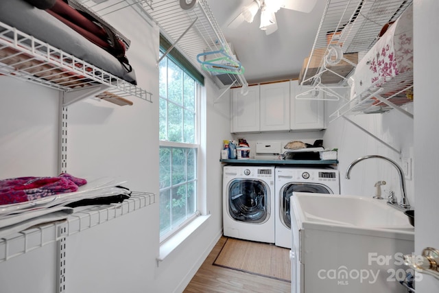 clothes washing area featuring cabinets, washing machine and dryer, plenty of natural light, and light hardwood / wood-style floors