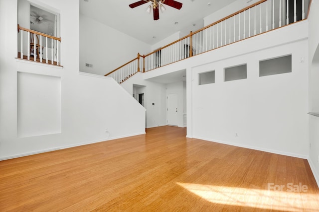 unfurnished living room with hardwood / wood-style flooring, a high ceiling, and ceiling fan