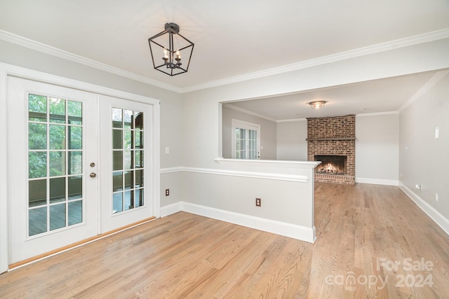 interior space featuring light wood-type flooring, french doors, ornamental molding, a brick fireplace, and brick wall