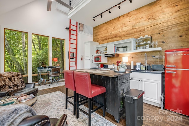 kitchen with a center island, white cabinetry, hardwood / wood-style flooring, rail lighting, and wooden walls