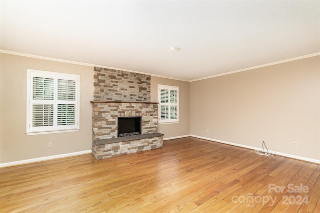 unfurnished living room with ornamental molding, a stone fireplace, and light wood-type flooring