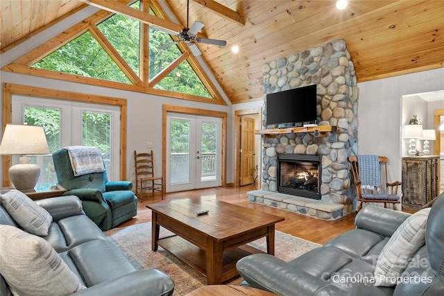 living room featuring a stone fireplace, french doors, light hardwood / wood-style floors, beam ceiling, and wooden ceiling