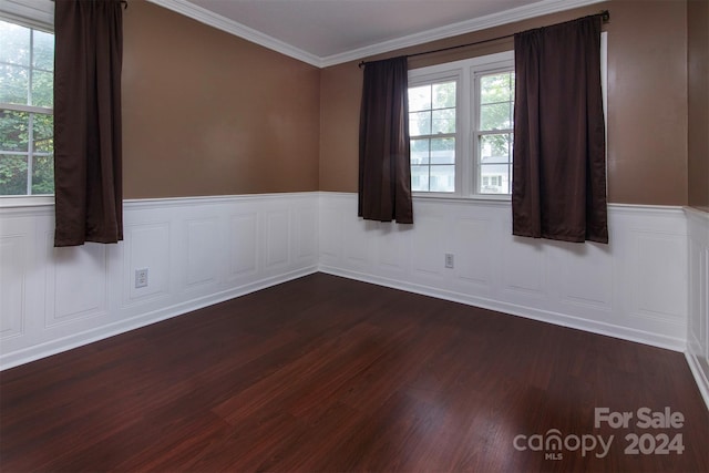 empty room featuring a wainscoted wall, plenty of natural light, dark wood finished floors, and crown molding