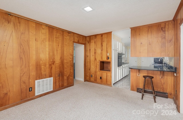 kitchen with wood walls, light colored carpet, a kitchen bar, and kitchen peninsula