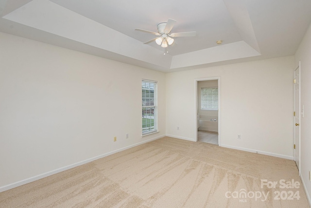 empty room with light colored carpet, ceiling fan, and a tray ceiling