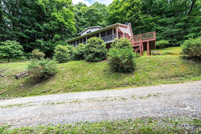 view of front of house with a deck, a wooded view, and a sunroom