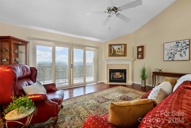 living area featuring wood finished floors, baseboards, a ceiling fan, vaulted ceiling, and a tiled fireplace