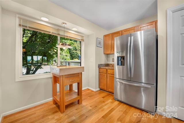 kitchen with light wood finished floors, hanging light fixtures, stainless steel fridge, and baseboards