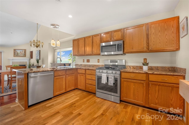 kitchen with a peninsula, a sink, a tile fireplace, stainless steel appliances, and light wood-type flooring