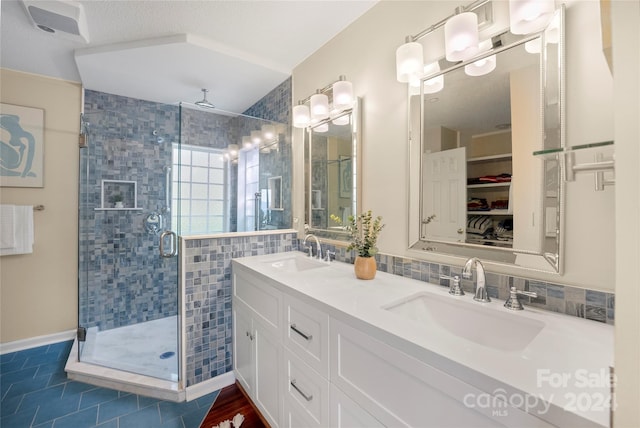 full bathroom with a sink, a spacious closet, a stall shower, and double vanity