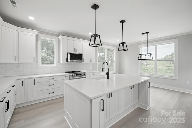 kitchen with sink, white cabinetry, stainless steel appliances, an island with sink, and decorative light fixtures