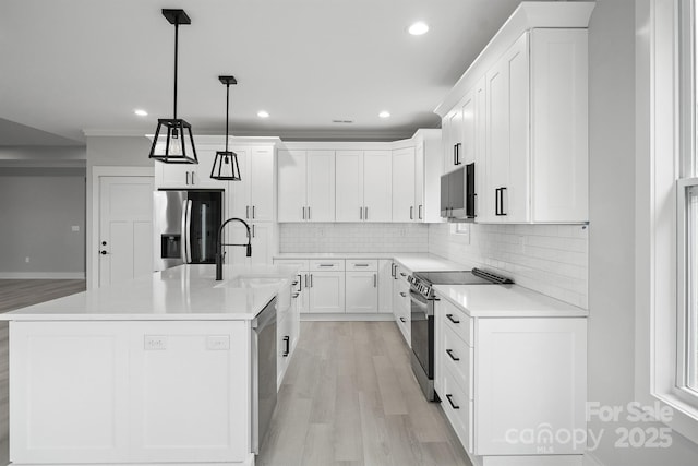 kitchen featuring decorative light fixtures, sink, white cabinets, a kitchen island with sink, and stainless steel appliances