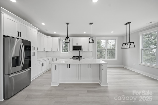 kitchen with appliances with stainless steel finishes, an island with sink, hanging light fixtures, and white cabinets