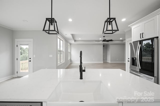 kitchen with pendant lighting, sink, stainless steel refrigerator with ice dispenser, light stone counters, and an island with sink