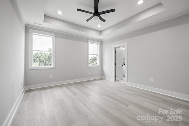 empty room with ceiling fan, light wood-type flooring, and a tray ceiling