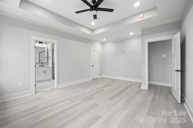 unfurnished bedroom with connected bathroom, sink, a tray ceiling, and light wood-type flooring