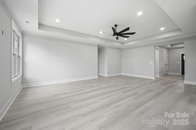 unfurnished living room with a raised ceiling, ceiling fan, and light wood-type flooring