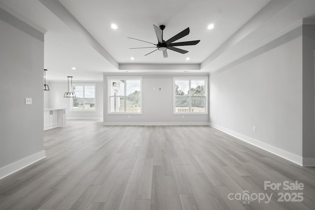 unfurnished living room featuring a raised ceiling, a wealth of natural light, and light hardwood / wood-style floors