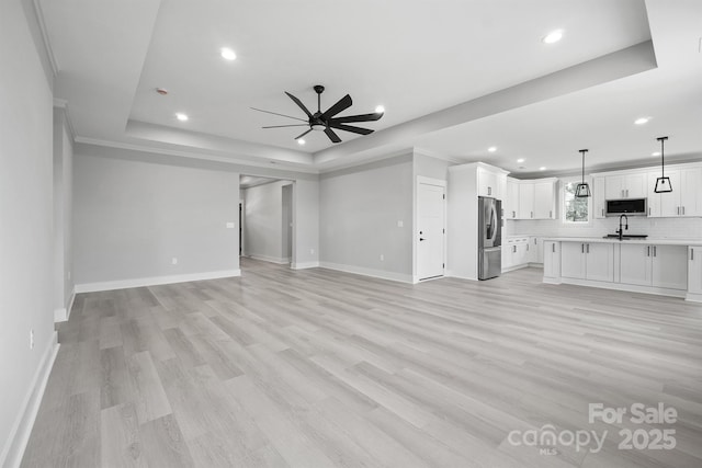 unfurnished living room featuring sink, a tray ceiling, light hardwood / wood-style flooring, and ceiling fan