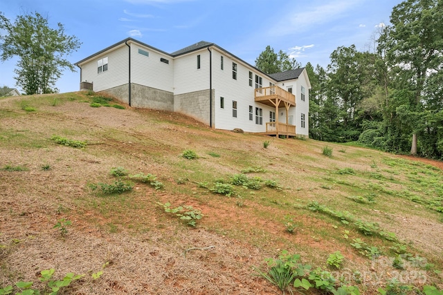 rear view of property featuring a wooden deck, a balcony, and a yard