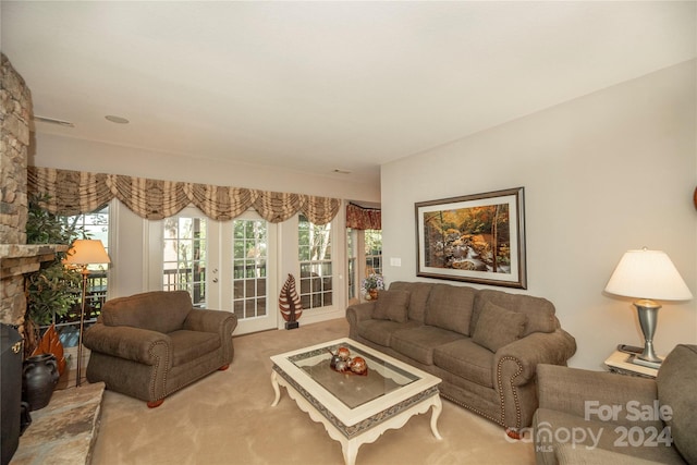 living room featuring french doors, light carpet, and a stone fireplace