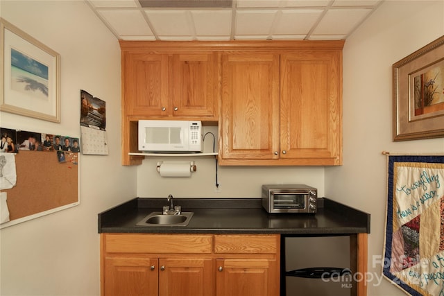 kitchen with a toaster, refrigerator, dark countertops, a sink, and white microwave