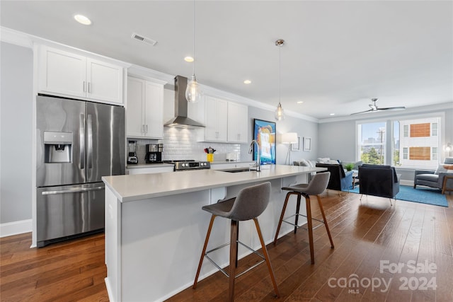 kitchen with appliances with stainless steel finishes, tasteful backsplash, wall chimney range hood, an island with sink, and dark wood-type flooring