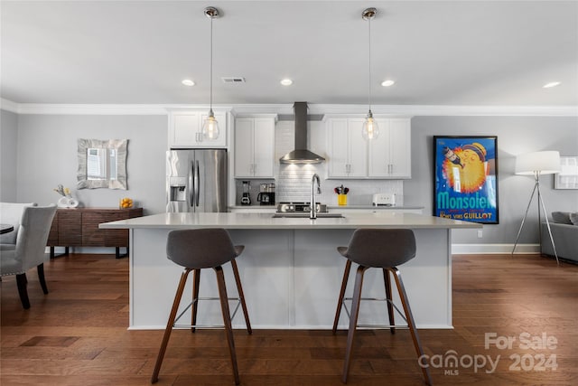 kitchen with dark hardwood / wood-style flooring, an island with sink, wall chimney exhaust hood, decorative backsplash, and stainless steel fridge