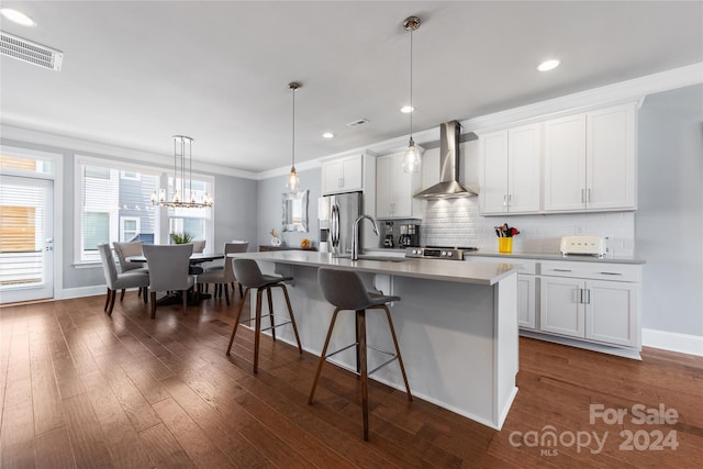 kitchen with a breakfast bar, white cabinets, stainless steel appliances, a center island with sink, and wall chimney exhaust hood