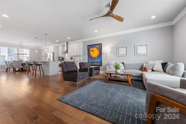 living room featuring ceiling fan with notable chandelier, crown molding, and dark wood-type flooring